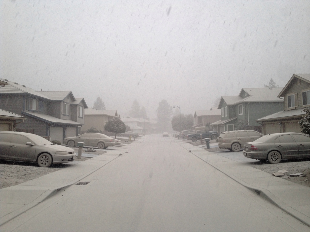 Volcanic ash covering cars and rooftops in a neighborhood, showing the grey accumulation and overcast sky during an ash fall event
